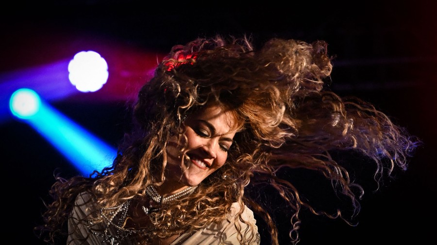 A performer shakes their long hair on stage while singing.