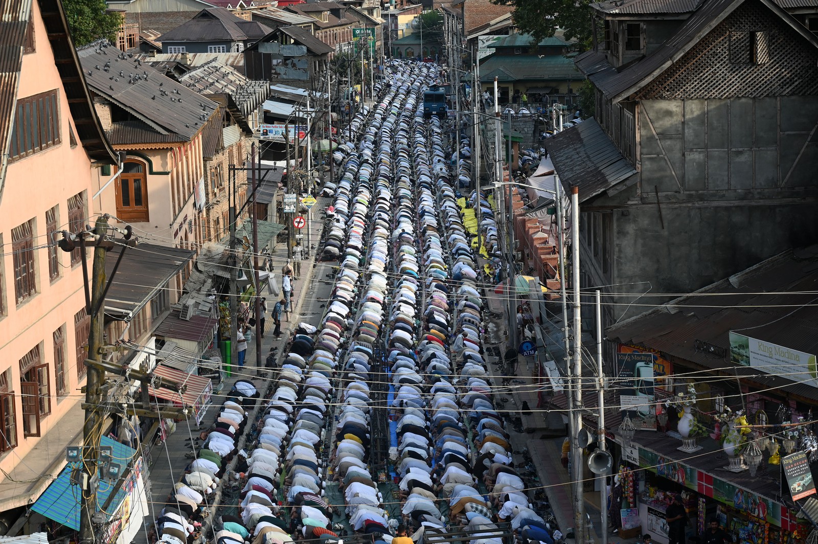 Rows of Muslim devotees kneel together in prayer, filling a street.