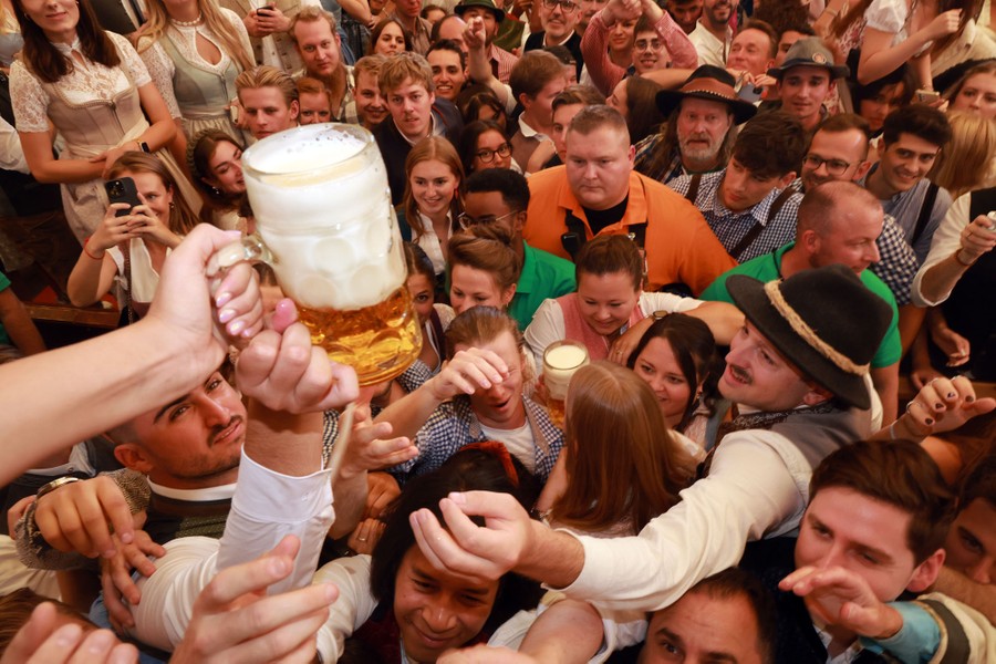 A crowd gathers close, with several people reaching up for a beer mug that is being handed out.