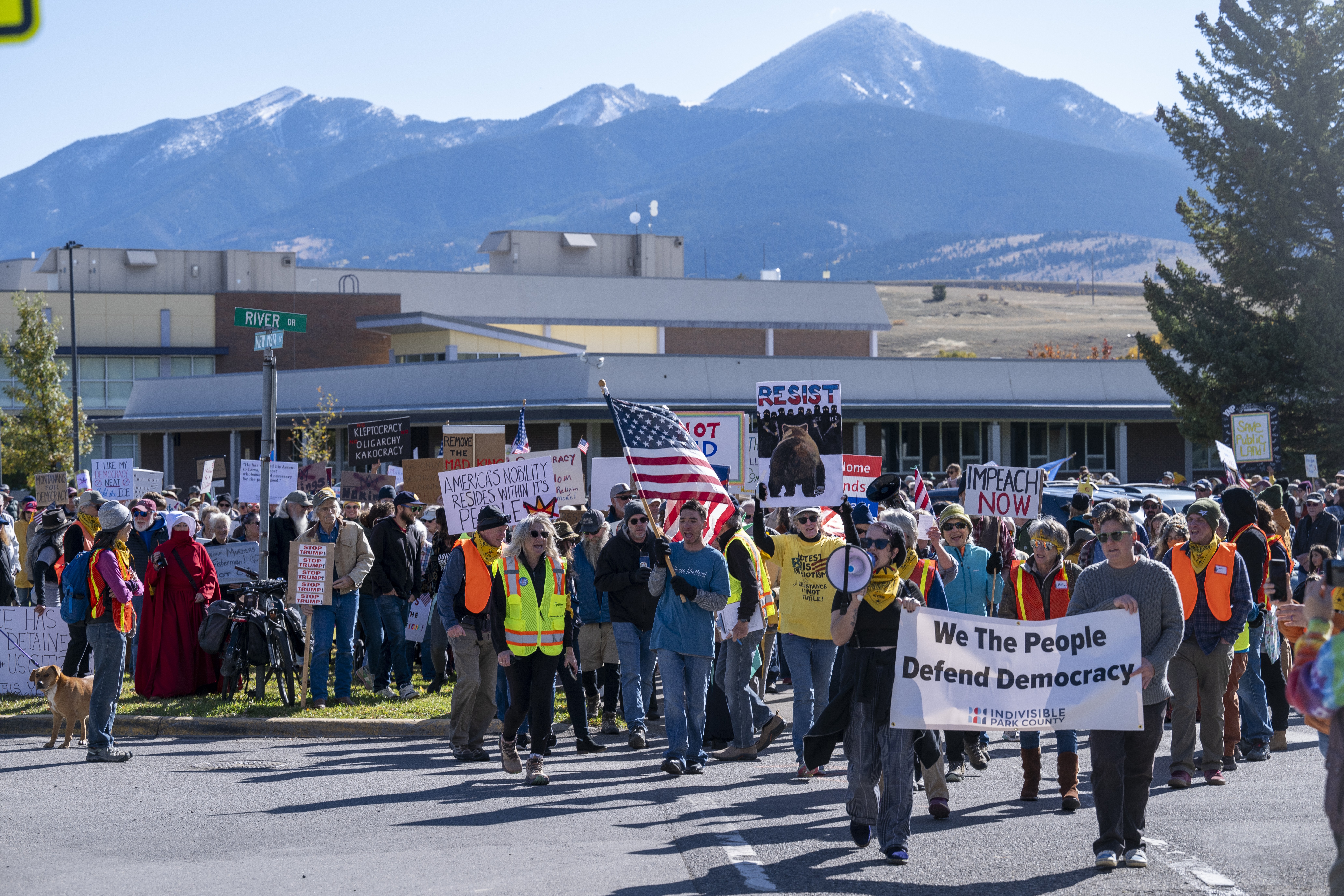 A group of protesters march in a Montana town, with mountains, visible in the background.