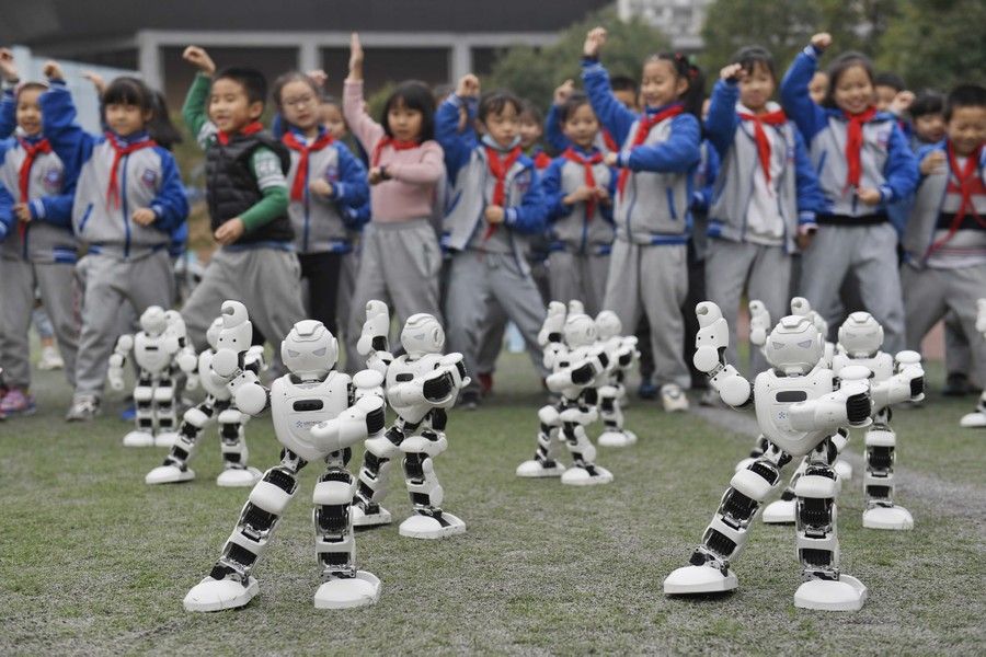 Children watch as small robots move in a group in front of them.