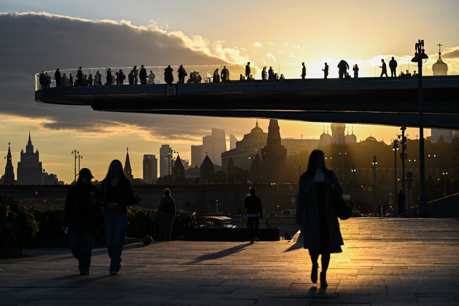 People stand on a cantilevered observation deck in Moscow, seen at sunset.