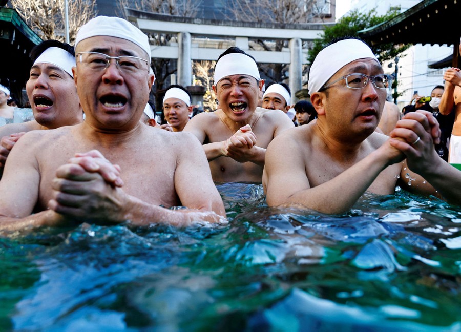 A group of shirtless men clasp hands and pray together while immersed in ice cold water.