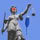 A sculpture of Lady Justice wearing a red blindfold and holding a bag of blue IV medicine