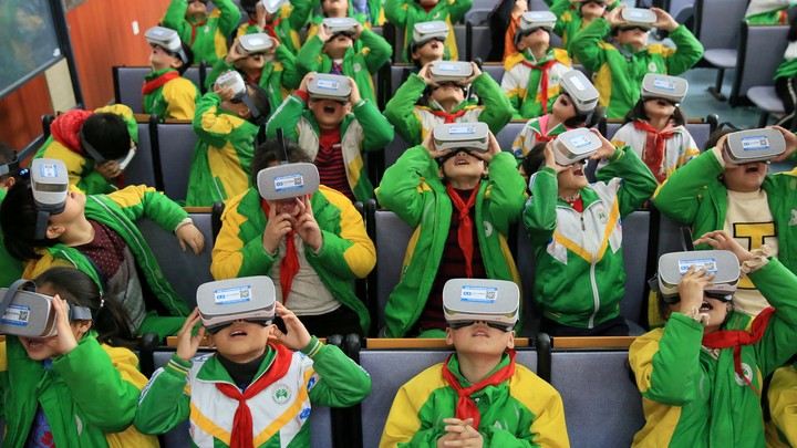 A group of kids in green and yellow school uniforms wearing VR headsets