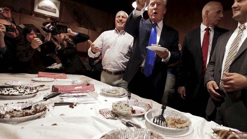 Donald Trump stands eating pie. 