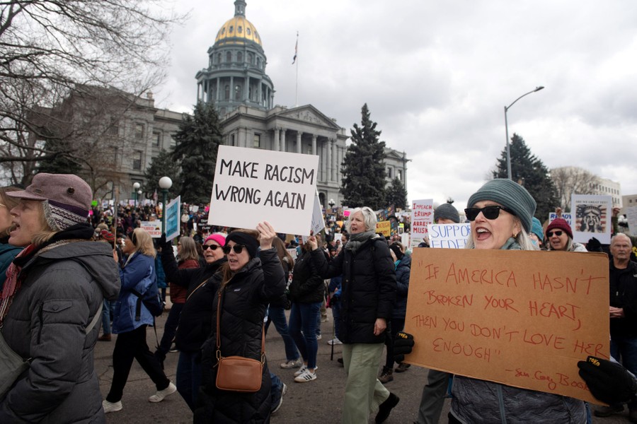 Protesters march past a state capitol building, carrying signs, including one that reads "Make racism wrong again."