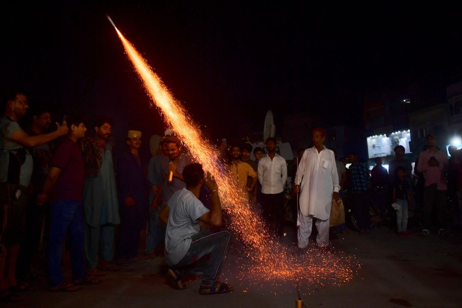 A group of men stand together and watch a small firework being launched.