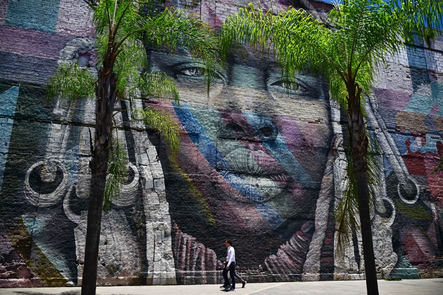 People walk past a large colorful mural of a face painted on a building's wall.
