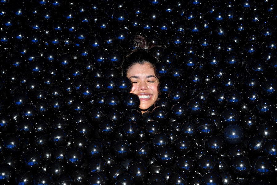 A person's face peeks through hundreds of small black plastic balls.