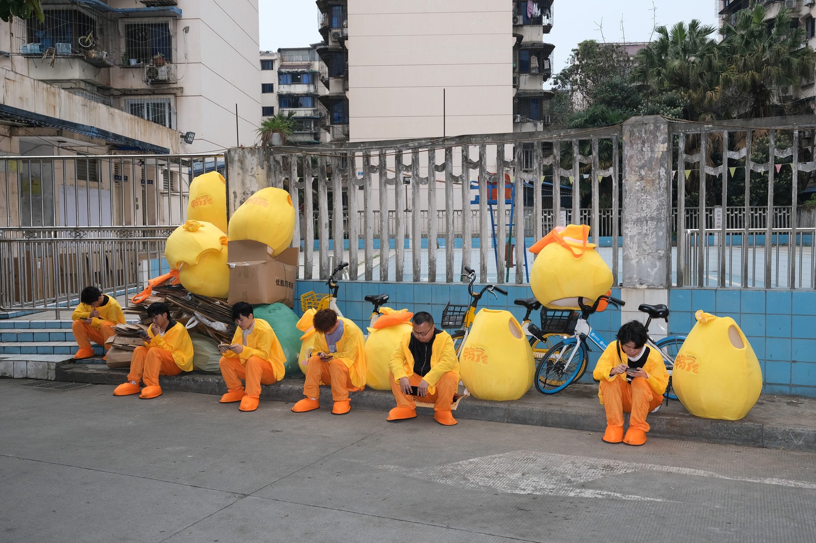 Costumed performers sit along a sidewalk, half-dressed, during a break.
