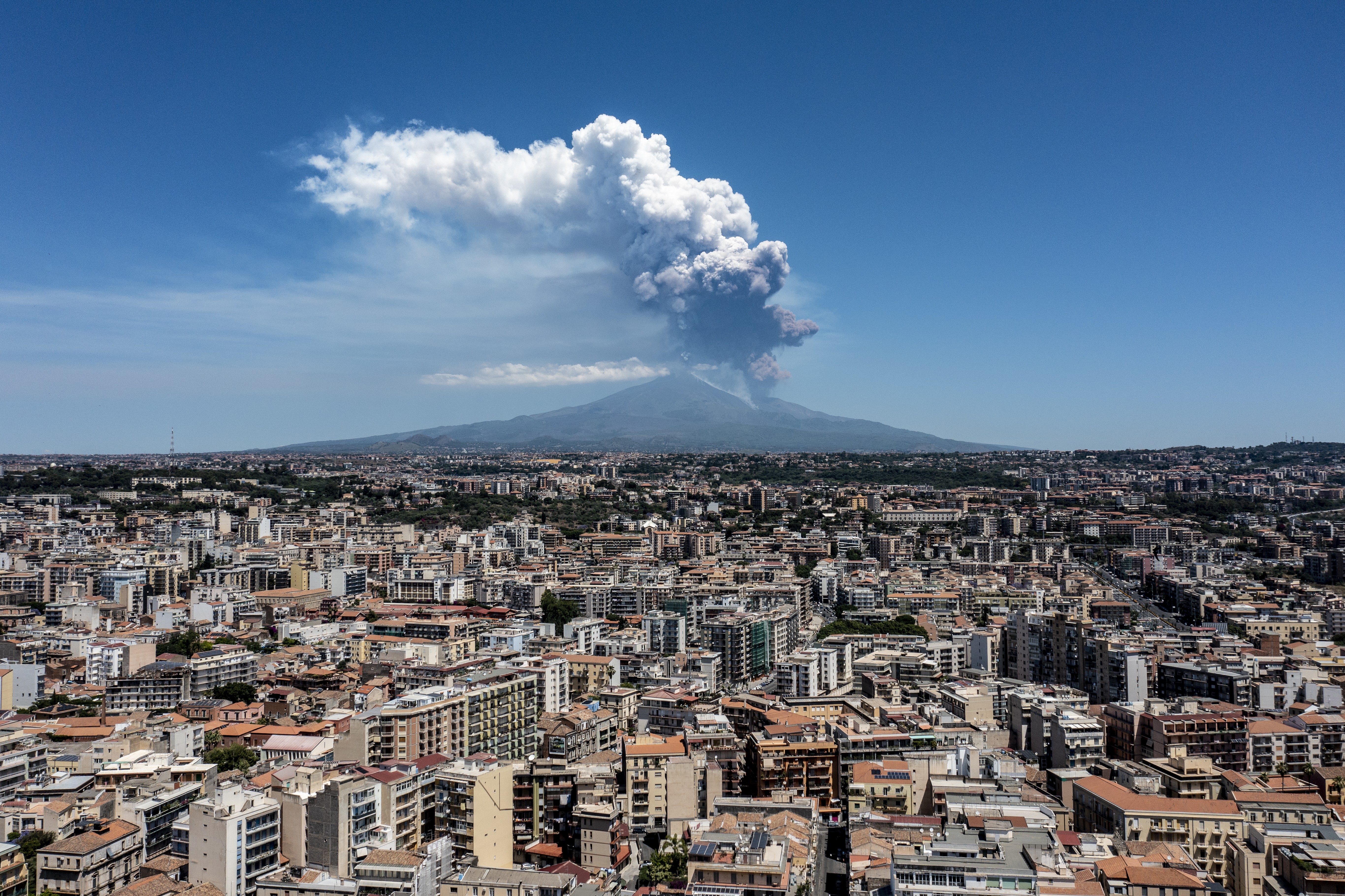 A broad view across city buildings, with an erupting volcano in the background.