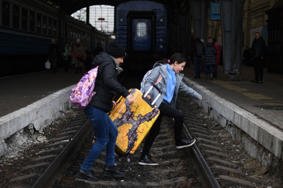 A family carries a large suitcase across train tracks in a train station.