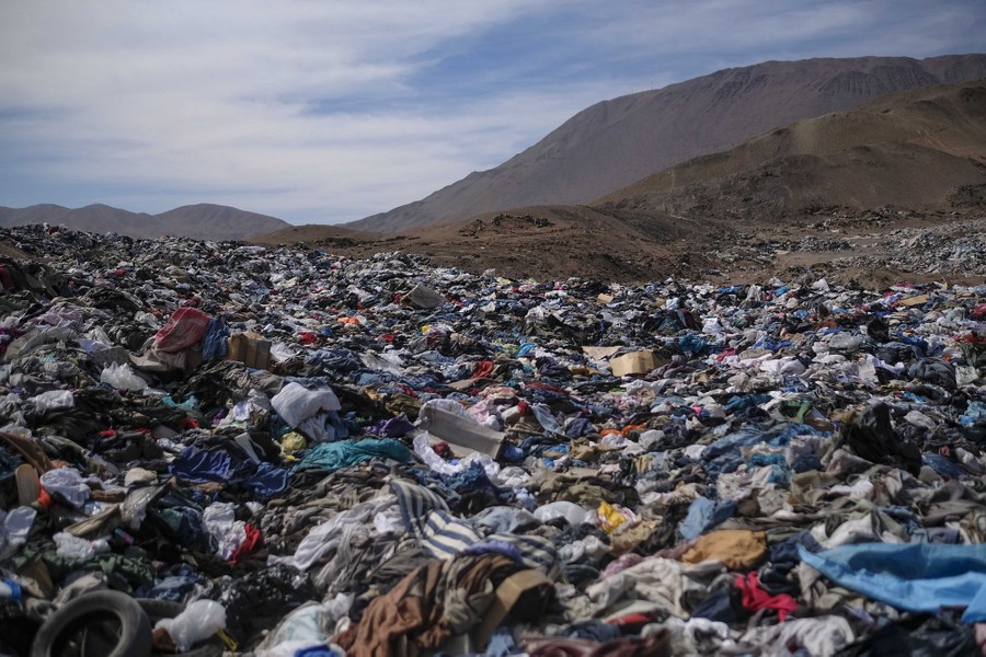 Broad piles of clothing lie strewn on the ground in an arid, mountainous area.