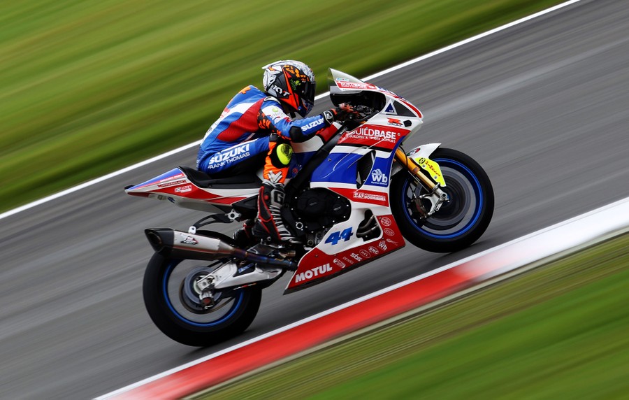 A racer rides a motorcycle on a track. The road and background appear blurred.