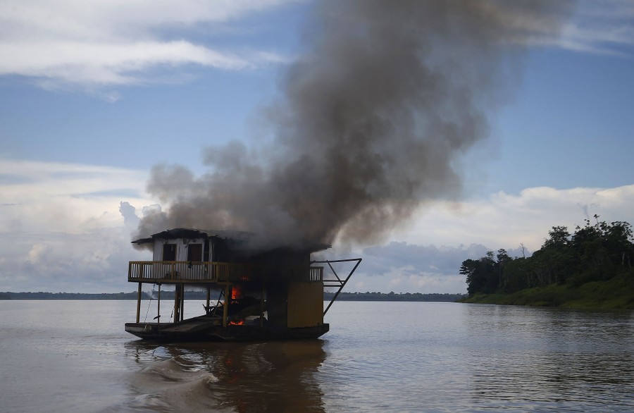 A burning two-story dredging barge floats in a river.