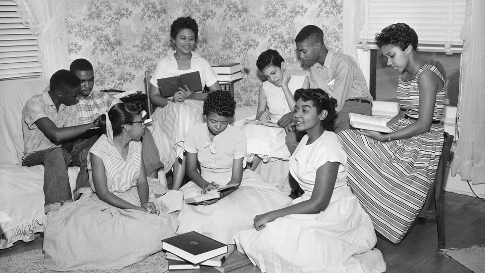 Nine students sitting on chairs and couches reading books in black and white