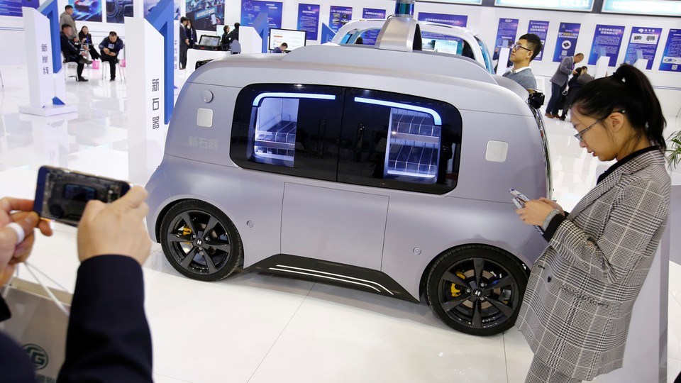 People stand indoors near a silver self-driving car