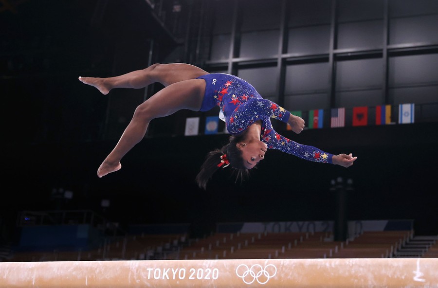 A gymnast leaps above a balance beam.