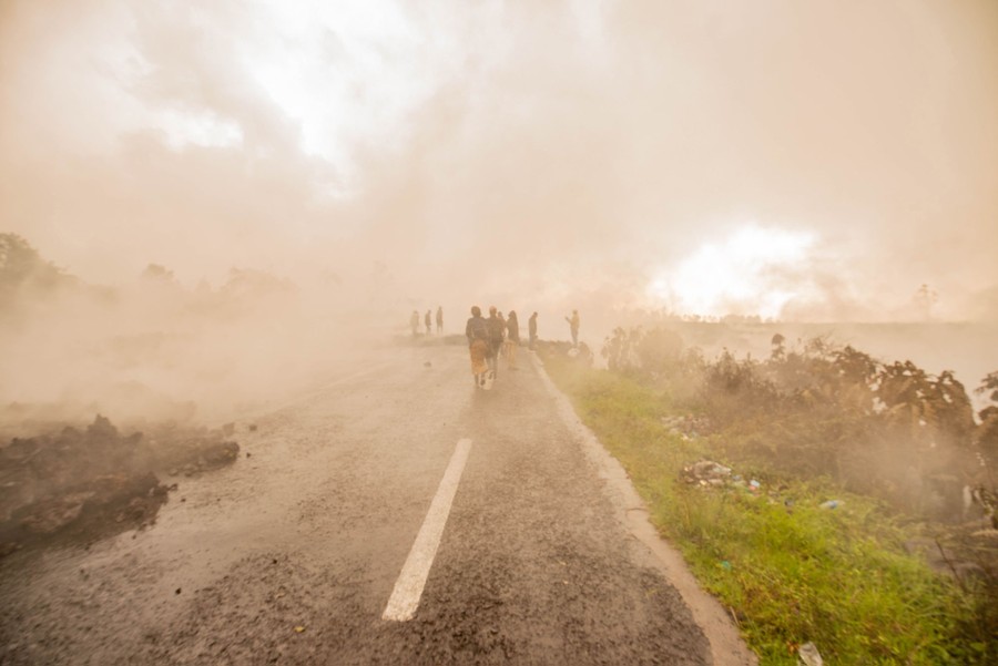 People walk on a road, engulfed in smoke and fumes from the nearby lava flow.