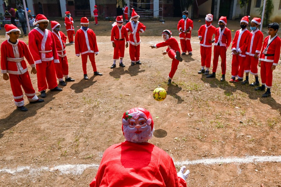 Children dressed as Santa Claus play with a soccer ball.