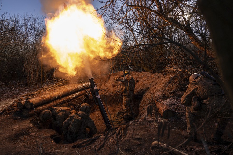 Soldiers fire a mortar from a ditch surrounded by trees.