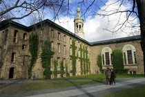 Two people walk past a brick, ivy-covered building on the Princeton University campus.