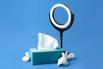 A staged photo of a ring light next to a box of tissues, with some used ones crumpled up nearby.