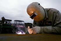 A welder works with a small torch and helmet on. 