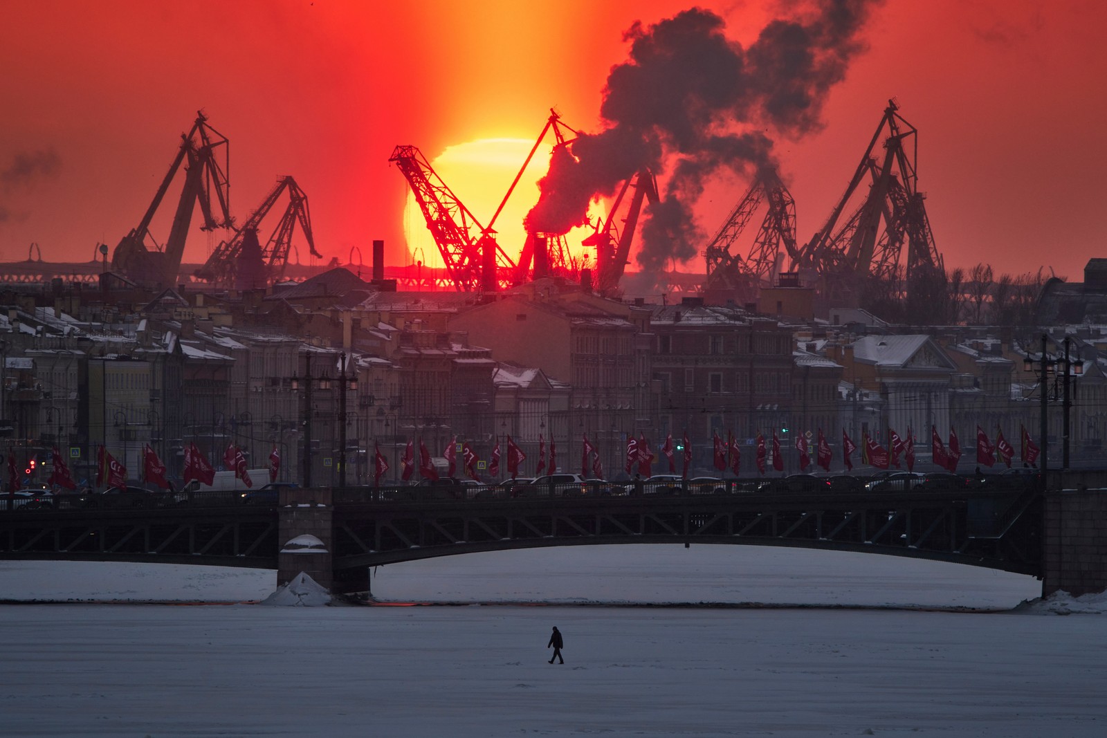 A bright sunset, viewed through industrial equipment and smokestacks.