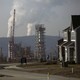 A smoking fracking project sits behind a suburban subdivision and beneath a gray, smoggy sky.