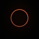 The moon appears in the sky directly in front of the sun, slightly smaller than the sun, forming a distinct orange ring in a dark sky.