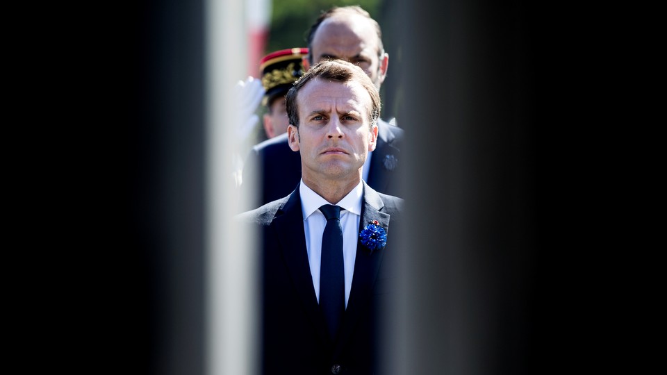 Emmanuel Macron stands framed between two doors with people lined up behind him.