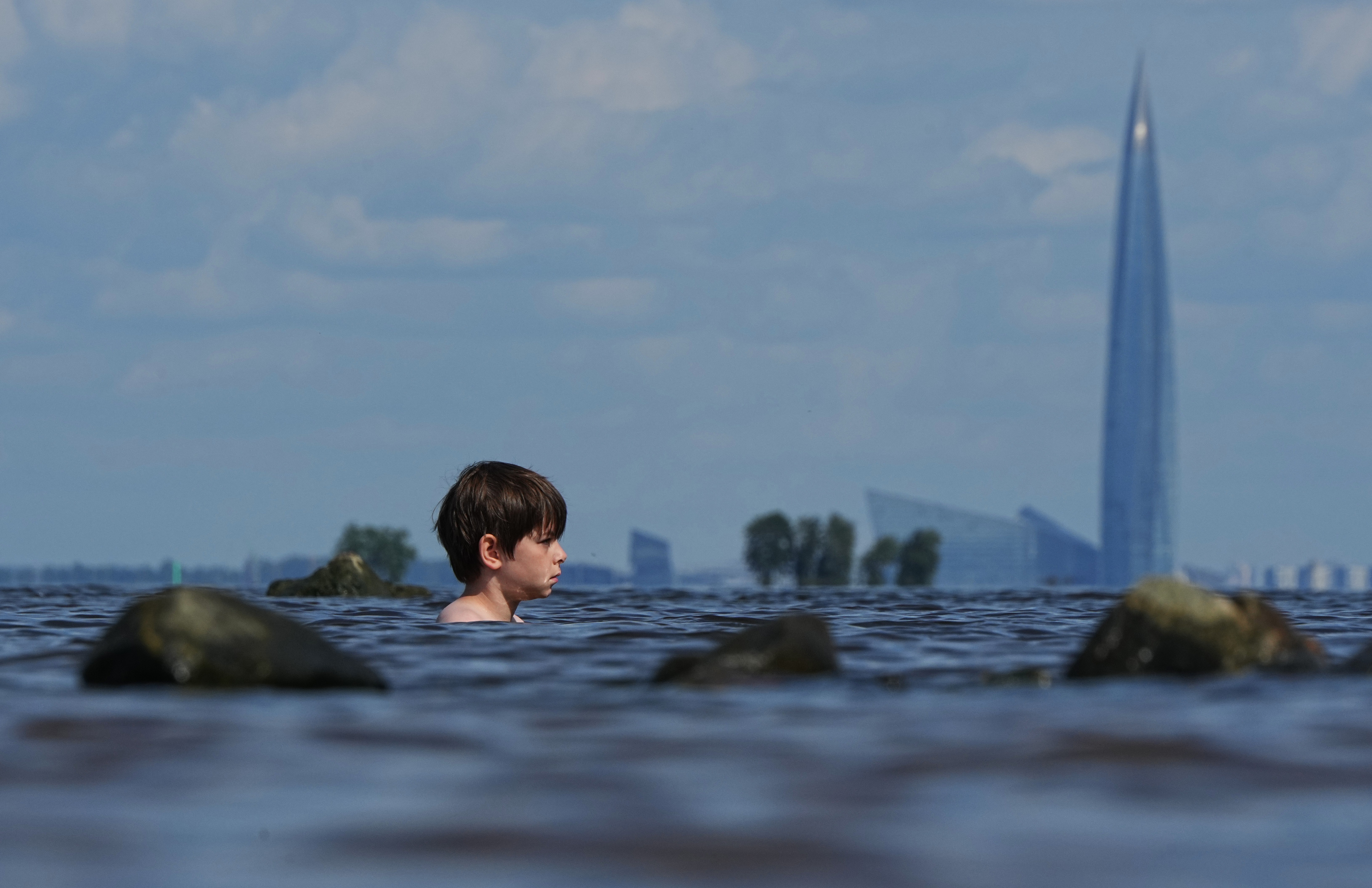 A boy floats in water, with a tall skyscraper visible in the distance.