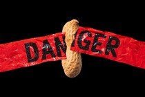 a peanut breaks through red "danger" tape against a black background