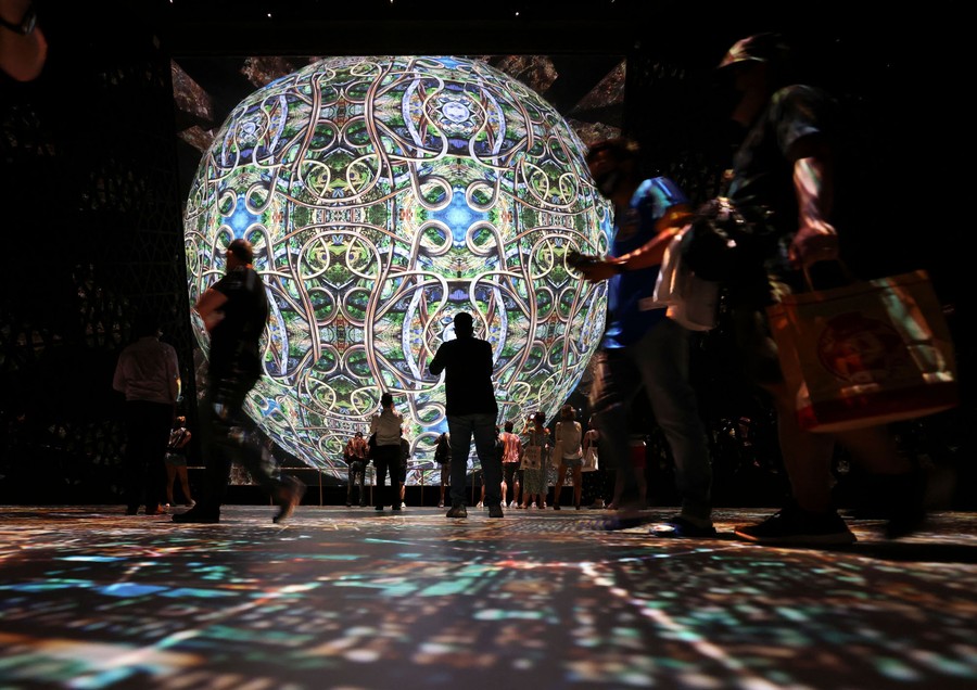 People stand next to a large illuminated sphere.