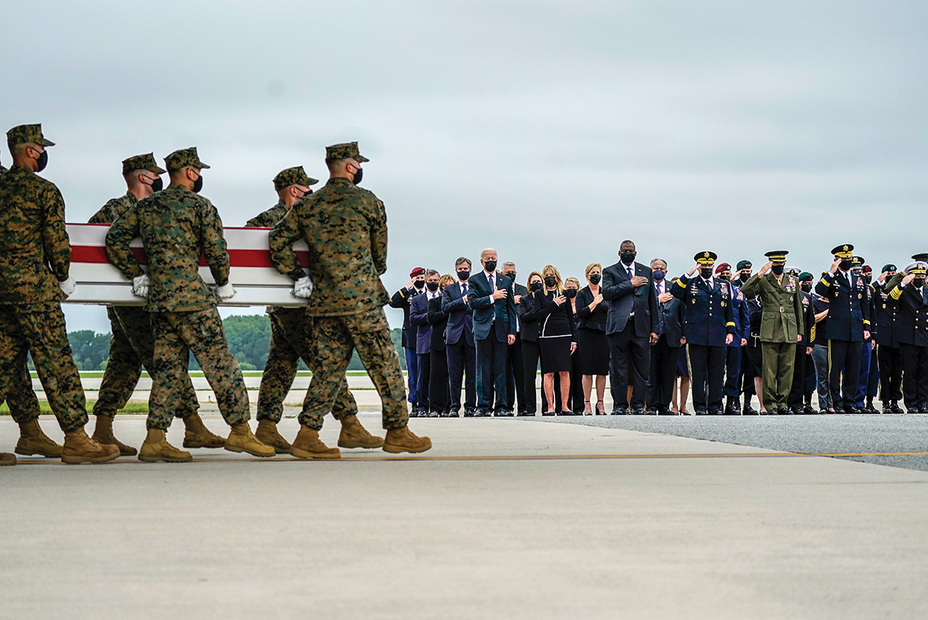 photo: Marines carry a flag-draped coffin on tarmac with a large group of people standing and saluting in background