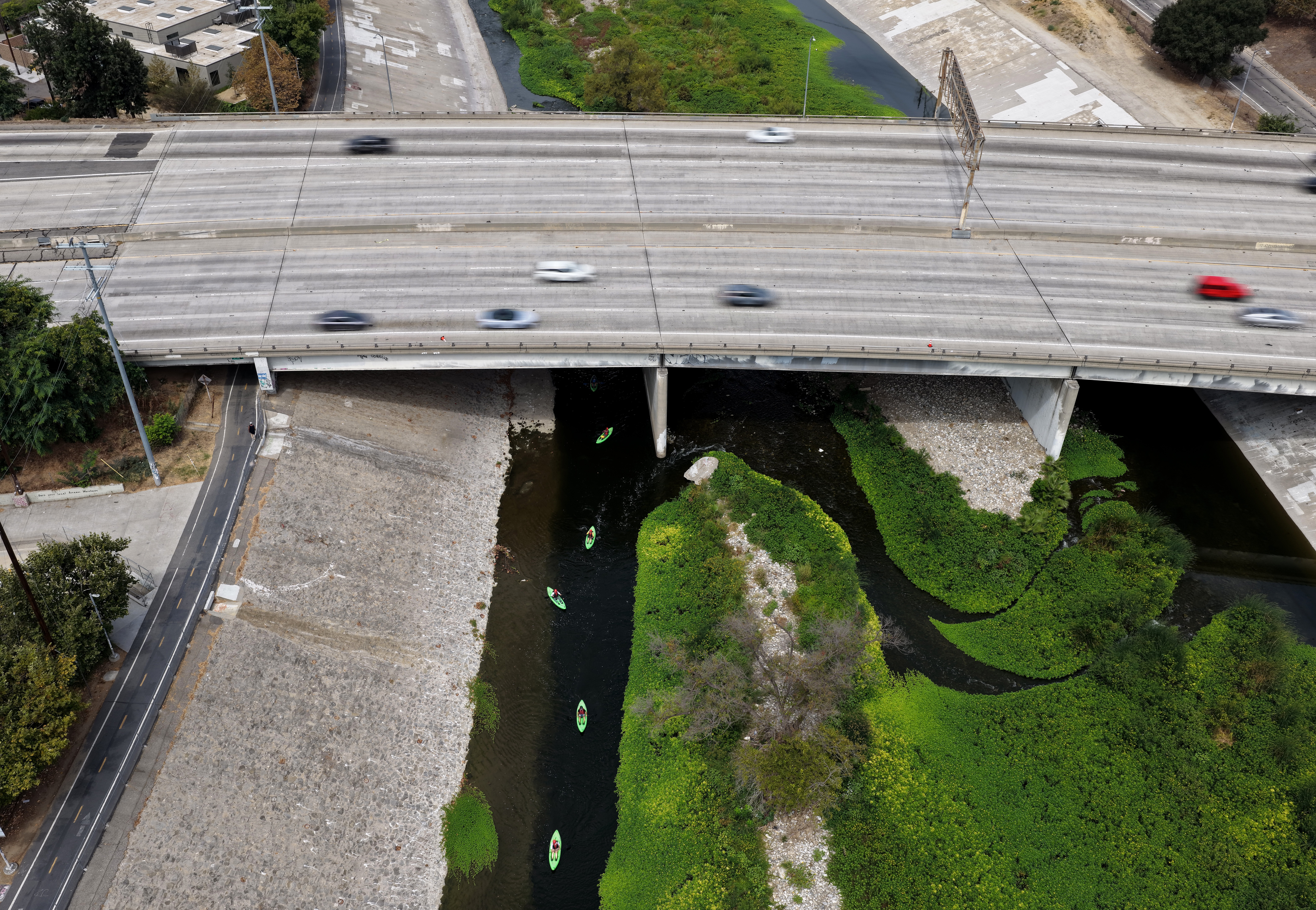An aerial view of traffic passing over the Los Angeles River as a kayak tour takes place below