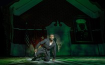 Actor in green light kneeling on ground with a knife