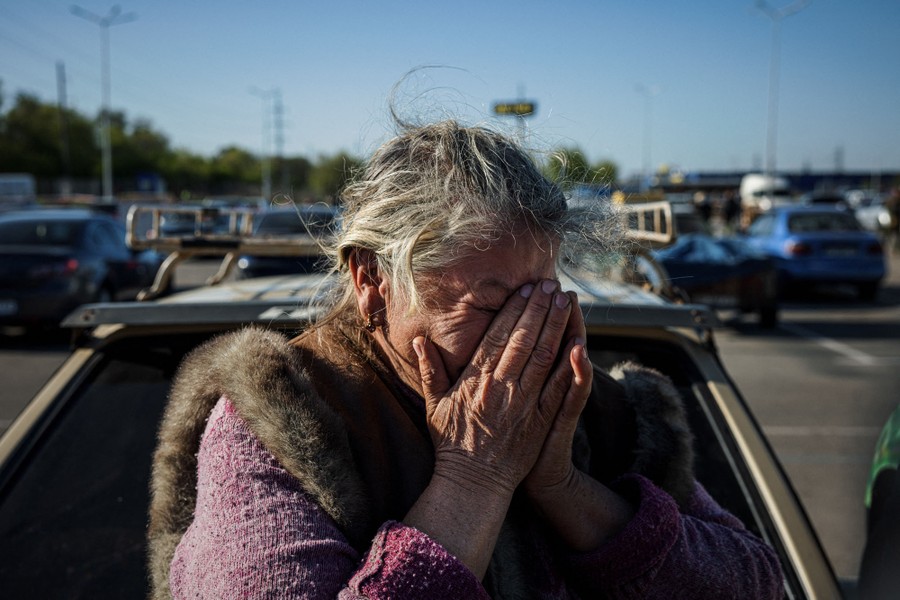 A woman holds her hands to her face, emotional, while standing in a parking lot.