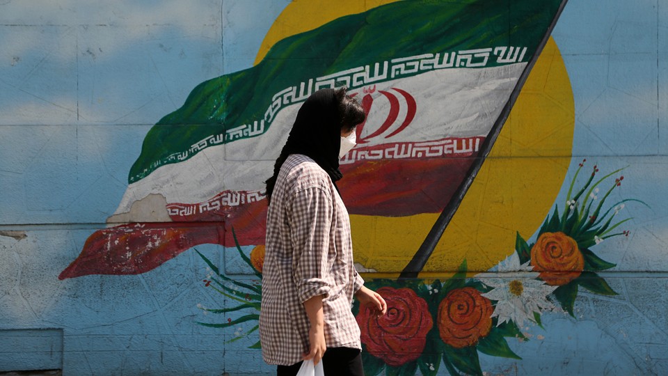 A woman walks in front of a mural of the Iranian flag