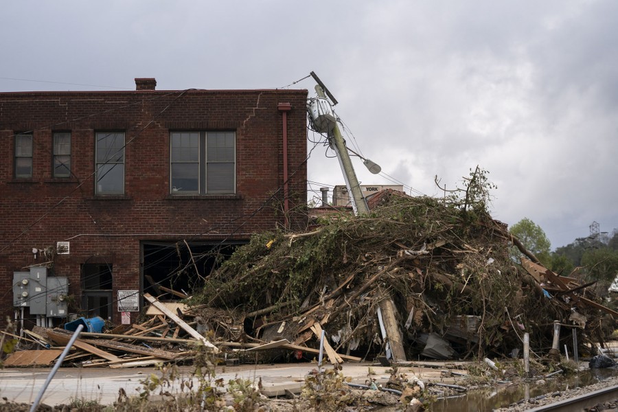 Piles of flood debris sit on a toppled power pole beside a building.