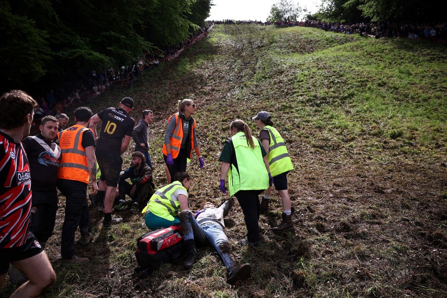 Race workers assist an injured runner who lies on their back at the bottom of a steep hill.