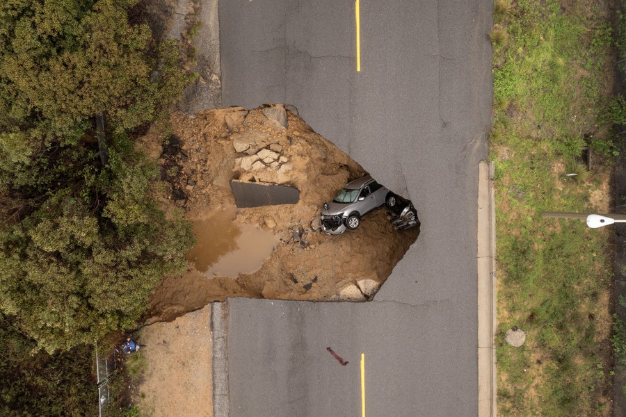 An aerial view of two vehicles in a sinkhole that opened up under a two-lane road.
