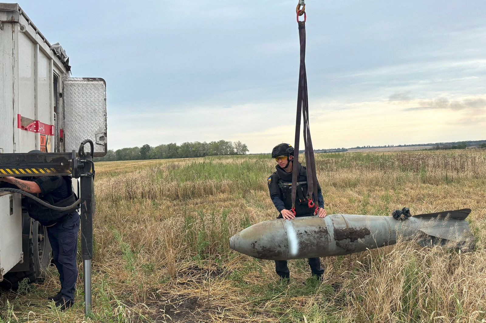 Workers use a sling to lift and remove a large unexploded bomb from a farm field.