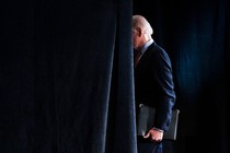 A photograph of Joe Biden walking behind a curtain