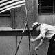 A black and white photograph of a man setting up an American flag on a New York City sidewalk in 1950