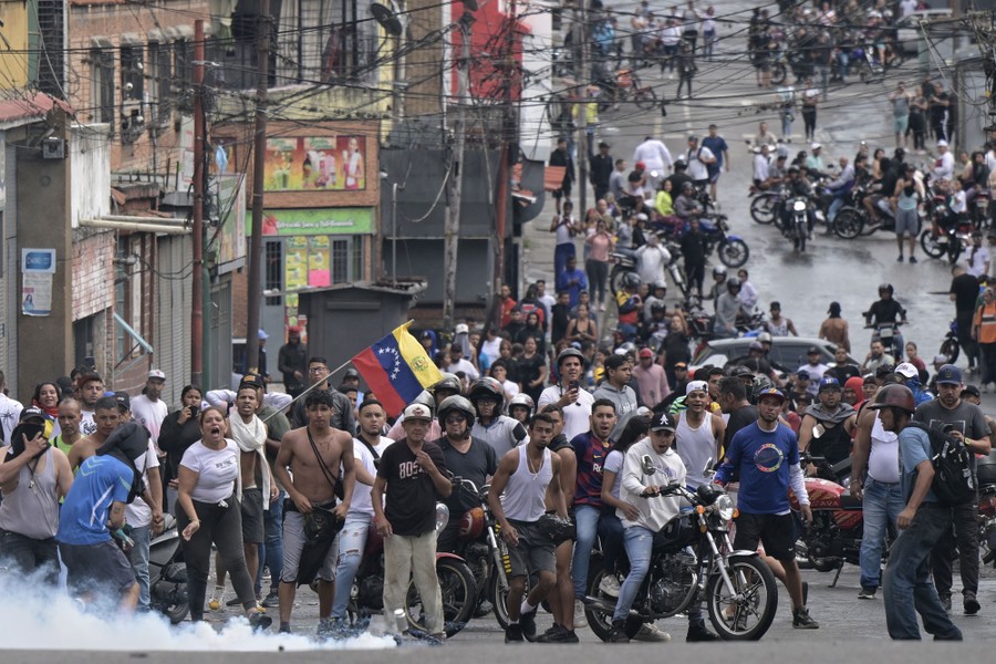 A crowd of protesters fills a street, some on motorcycles.