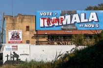 A “Vote Kamala” advertisement hangs defaced with “Trump” graffiti near a mural for fallen soldiers on Election Day in Philadelphia.