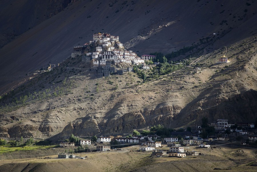 A cluster of buildings sits on a hilltop on a fairly barren mountainside.